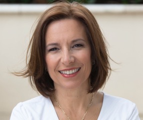 Bio photo of Sara Pizano smiling, in a white shirt in a sunlit setting